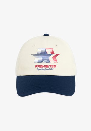 Jonge man die een beige en marineblauwe pet draagt met een vlaglogo, een marineblauwe jas met borduursel "Modern Yuppies" en een grijs overhemd met een rood en blauw ontwerp.