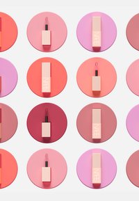 Des produits de lèvres disposés sur des cercles colorés, présentant différentes nuances de rose, corail et rouge. Chacun a un contenant rectangulaire avec un applicateur en wand.