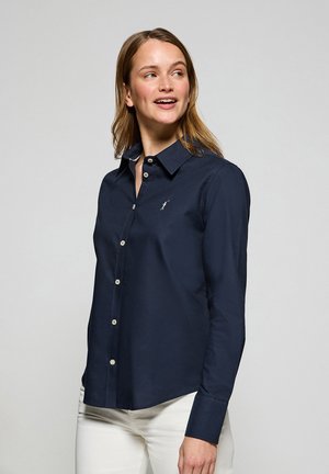 Marineblauwe button-up shirt van een zachte stof met een spitse kraag en witte knoopaccenten. Bevat een klein geborduurd logo op de borst.