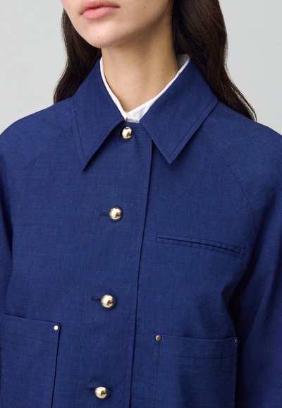 Veste boutonnée bleu marine en tissu texturé, dotée de boutons dorés, de deux poches avant et d'un col pointu.