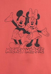 Camiseta coral con un gráfico impreso en negro de Mickey y Minnie Mouse tomados de la mano, con el texto en negrita "MICKEY MINNIE" debajo.