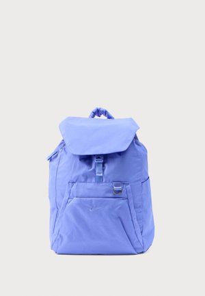 Sac à dos violet clair avec rabat avant, petite poche zippée à l'avant, poignée supérieure et anneau en D argenté sur fond uni.