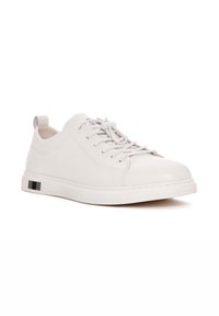 Sneaker in pelle bianca con punta rotonda, chiusura con lacci e sottili dettagli testurizzati. Presenta una sottile striscia nera sulla suola.