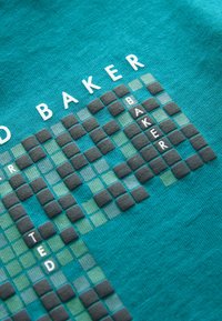 Tyrkysová textilie s designem křížovky v tmavě šedé a bílé barvě, s texturovanými čtverci a písmenkovými akcenty, které tvoří jména "Baker" a "Ted."