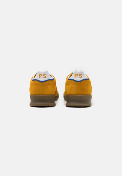 Yellow suede sneakers with a low profile, brown rubber sole, white heel tab, and blue accents. "PS" logo in orange on the heel.