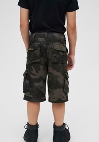 Khaki kapsáče v tmavě zelené a černé barvě, se bočními kapsami, volným střihem a ohrnutými lemy, doplněné černými šněrovacími botami.