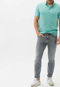 Polo shirt blu chiaro con due bottoni, abbinato a jeans grigi slim-fit e sneakers bianche con accenti grigi. Texture liscia, design casual.