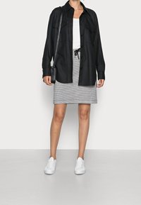 Camicia nera button-up con due tasche sul petto, abbinata a una mini gonna grigia a quadri e sneakers bianche, con vita regolabile e design elegante.