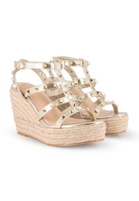 Sandalias cuña metálicas doradas con tiras con tachuelas, suela envuelta en yute y forro interior suave. Hebilla ajustable en el tobillo para un mejor ajuste.