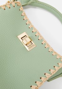 Green textured leather handbag featuring beige woven accents and a gold-tone clasp closure. Smooth surface with pronounced stitching details.