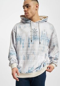 Sudadera con capucha en gris claro con patrones geométricos azules, bolsillo tipo canguro y puños de canalé. Presenta un gráfico de una palmera en el pecho.