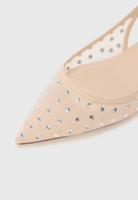 Nude mesh pointed-toe flats adorned with metallic silver round studs, featuring a transparent polka dot panel on the sides.