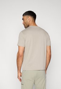 Μπεζ κοντομάνικη μπλούζα με στρογγυλή λαιμόκοψη. Μαλακό ύφασμα, άνετη εφαρμογή, απλό σχέδιο, χωρίς ορατά μοτίβα, φορεμένη με ανοιχτό πράσινο παντελόνι.