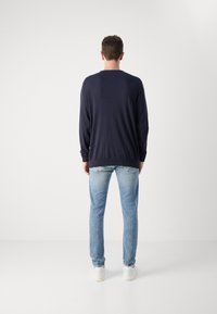 Tamsiai mėlynas megztinis ilgomis rankovėmis ir apvalia iškirpte, derinamas su šviesiai mėlynomis džinsais. Baltos sportbačiai užbaigia įvaizdį. Paprastas ir kasdienis dizainas.