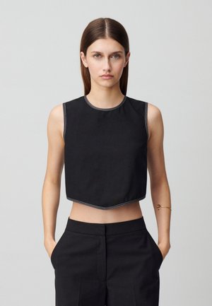 Top cropped nero con scollatura rotonda e cuciture bianche lungo i bordi, abbinato a pantaloni neri a vita alta.