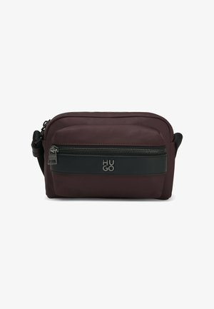 Czerwona i czarna tekstylna torba na ramię z zapięciem na suwak, posiadająca przednią kieszeń oraz wytłoczone logo na czarnym pasku. Gładka faktura.