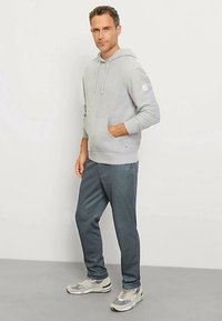 Gray hooded sweatshirt with front pocket, paired with dark gray jogger pants. Model wears light gray sneakers. Simple, casual athletic look.