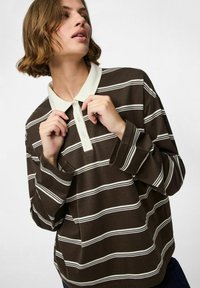 Bruin gestreepte langemouwen polo shirt met een witte kraag en knopenlijst. Heeft horizontale witte strepen en een losse pasvorm.