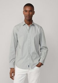 Camicia a righe in verde chiaro e bianco, realizzata in cotone. Presenta un colletto, maniche lunghe e un orlo curvo con etichetta del logo.