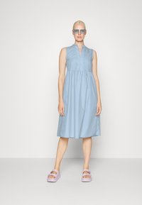 Vestido sem mangas azul-claro com decote colarinho e detalhes de botões; saia rodada. Combinado com sandálias de plataforma lavanda.