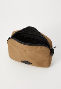 Borsetta zip in tessuto beige, con zip nera e tasche interne. Toppa con logo nera sul davanti, design rettangolare con bordi arrotondati.