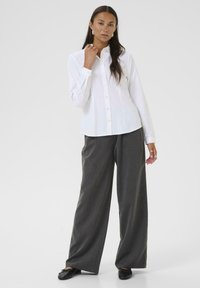 Chemise blanche à boutons, à manches longues et col, associée à un pantalon large gris et des ballerines noires. Design simple et structuré.