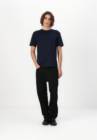 Camiseta de manga corta azul marino en un corte relajado, combinada con pantalones de pierna ancha negros. Los zapatos son negros, con un diseño minimalista.