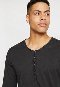 Zwarte lange mouwen henley shirt met een ronde hals, vijfknopssluiting en een zachte, gestructureerde stof.