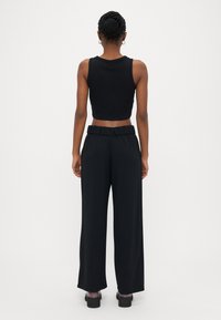 Schwarzes, kurzes Tanktop mit rundem Ausschnitt, kombiniert mit weiten schwarzen Hosen mit elastischem Bund. Dazu getragen werden klobige schwarze High Heels.