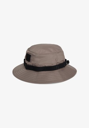Chapeau seau marron clair avec large bord et sangle réglable noire autour de la base, présenté sur un fond blanc.