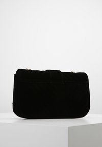 Svart sammetshandväska med ett kviltat mönster, som har en strukturerad rektangulär form och ett kort handtag. Guldhardware accenter är synliga.