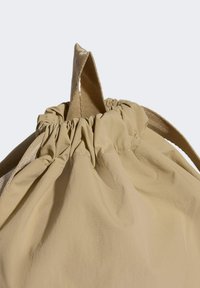 Bolsa beige con cordón hecha de tela suave, con parte superior fruncida, correas gruesas y una superficie lisa y texturizada.