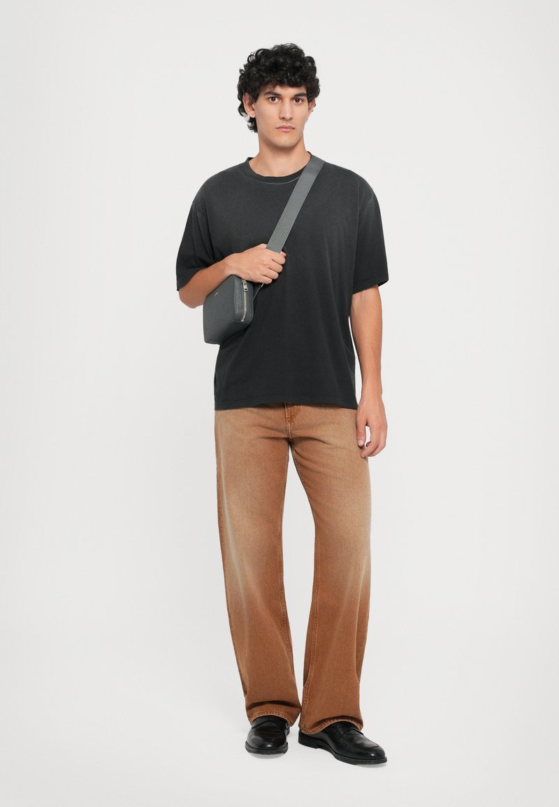 Black oversized t-shirt, light brown wide-leg jeans, black shoes, and a gray crossbody bag with a zipper, on a neutral background.