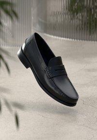 Schwarze Lederloafers mit einer gesteppten Akzentuierung an der Spitze und flachem Absatz. Glatte Textur mit minimalistischem Design.