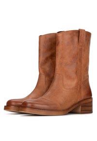 Bottines en cuir tan avec une finition lisse, bout rond et petit talon empilé. Présente des détails sur les coutures latérales et une languette pour un enfilage facile.