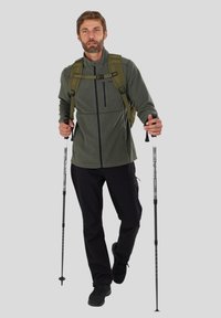 Green fleece jacket with a zippered pocket, black pants, and trekking poles, worn with an olive green backpack. Outdoor gear suitable for hiking.
