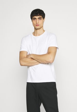 White cotton t-shirt with a round neck, short sleeves, and a relaxed fit, paired with black trousers. Simple design, no patterns or graphics.