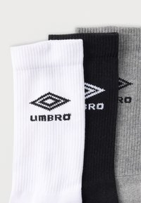 Trzy pary sportowych skarpet w kolorach białym, czarnym i szarym. Prążkowana faktura z logo w kształcie diamentu i nazwą marki "Umbro".