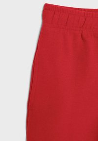 Rdeče hlače iz tkanine z elastičnim pasom in šivi na stranskih žepih na svetlo sivi podlagi, prikazana zgornja leva sekcija.