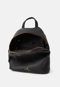 Sac à dos en cuir noir avec une texture lisse, fermeture zippée dorée et logo sur le devant. Il dispose d'un compartiment ouvert avec une poche intérieure zippée.