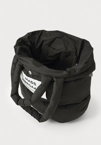 Sac matelassé noir avec une texture douce, une forme arrondie et deux anses épaisses. Présente un patch logo blanc sur un côté.