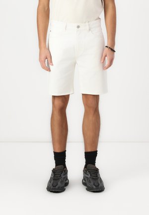 Shorts in denim bianco con taglio dritto, design a cinque tasche e chiusura con bottone in metallo. Abbinati a calze nere e sneakers camouflage.