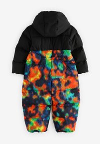 Fodrad sn overall med en svart överdel och en texturerad huva samt färgglada, prickiga byxor i mönster som blandar orange, grönt och blått.