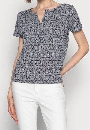 Navy blouse with white paisley pattern, short sleeves, V-neck, lightweight fabric, paired with white pants.