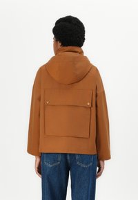Veste à capuche marron avec une poche à l'arrière, manches longues et coupe décontractée. Fabriquée en tissu léger et texturé.