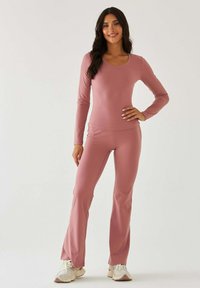 Różowy dres z długim rękawem z dekoltem w serek i dopasowanym topem, połączony z rozszerzanymi spodniami; miękka tekstura i elastyczny materiał.