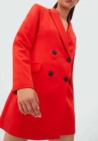 Rode double-breasted blazer gemaakt van gladde stof, met zwarte knopen, scherpe revers en zijzakken. Korte, getailleerde pasvorm.