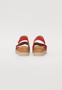 Sandales en suède rouge avec un talon en liège recouvert, des sangles réglables et une semelle intérieure lisse beige. Semelle plate pour la stabilité et le confort.