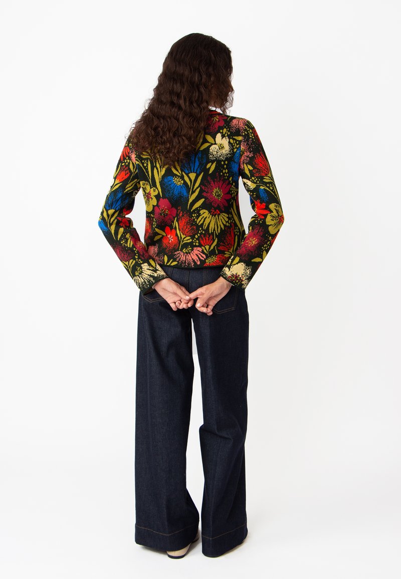 Haut en tricot à manches longues avec motif floral, aux couleurs vives sur fond noir, associé à un pantalon large en denim noir.