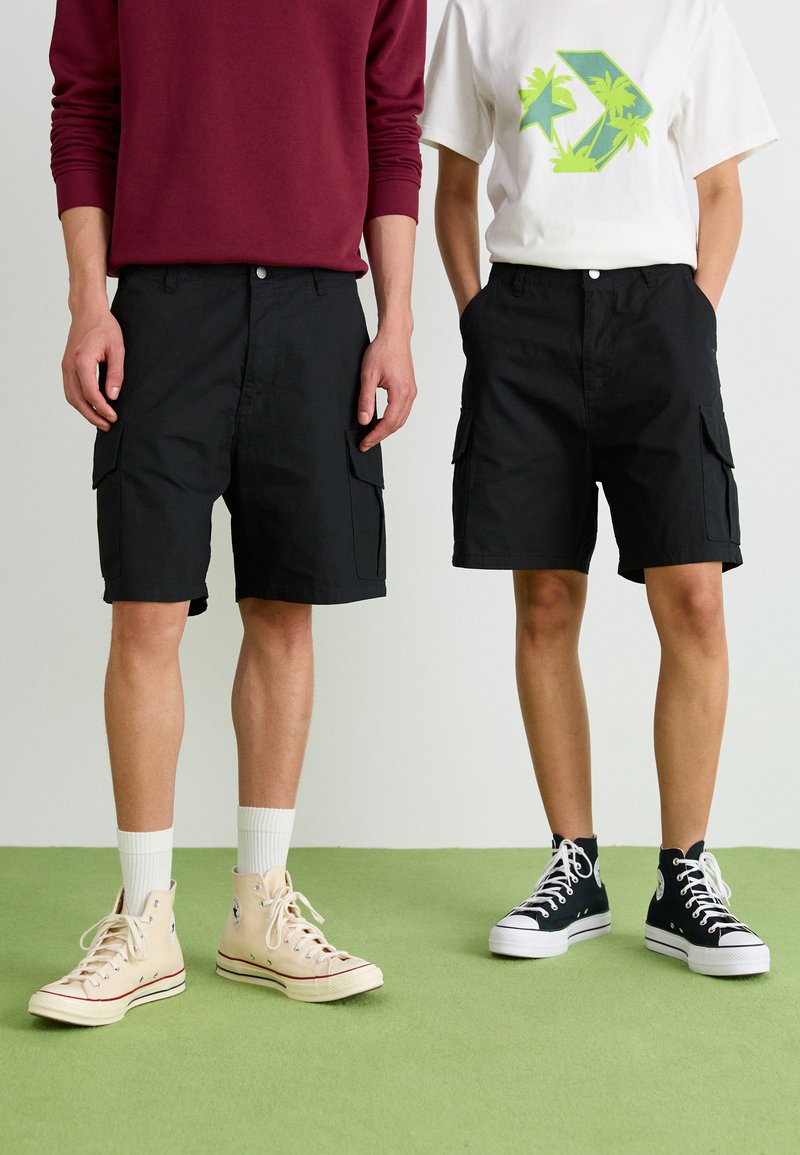 Sorte cargoshorts med sidelommer, parret med en hvid grafisk t-shirt og en bordeaux sweatshirt, båret med høje sneakers.